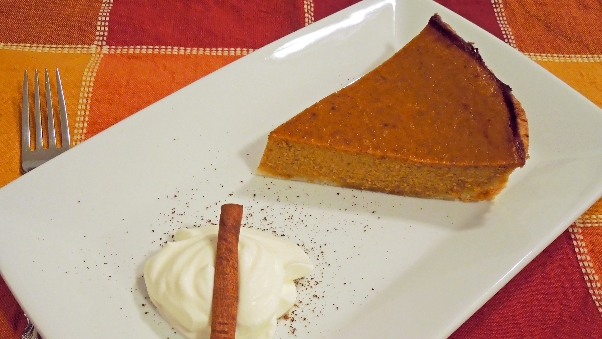 Pumpkin Pie on a fall-colored placemat. Plate garnished with whipped cream and cinnamon stick.